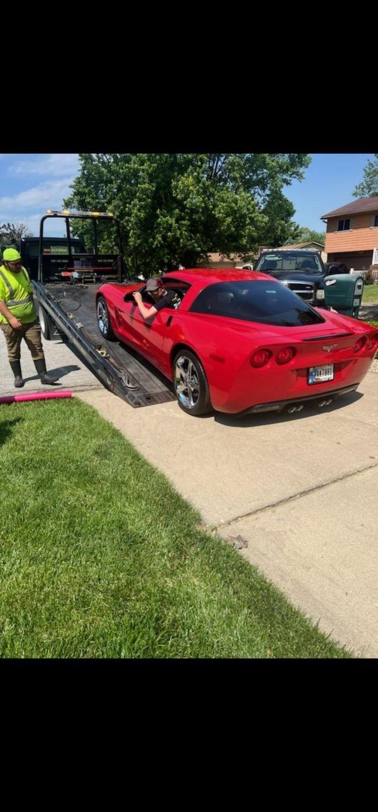 A red sports car being loaded onto a tow truck on a suburban street in sunny weather.