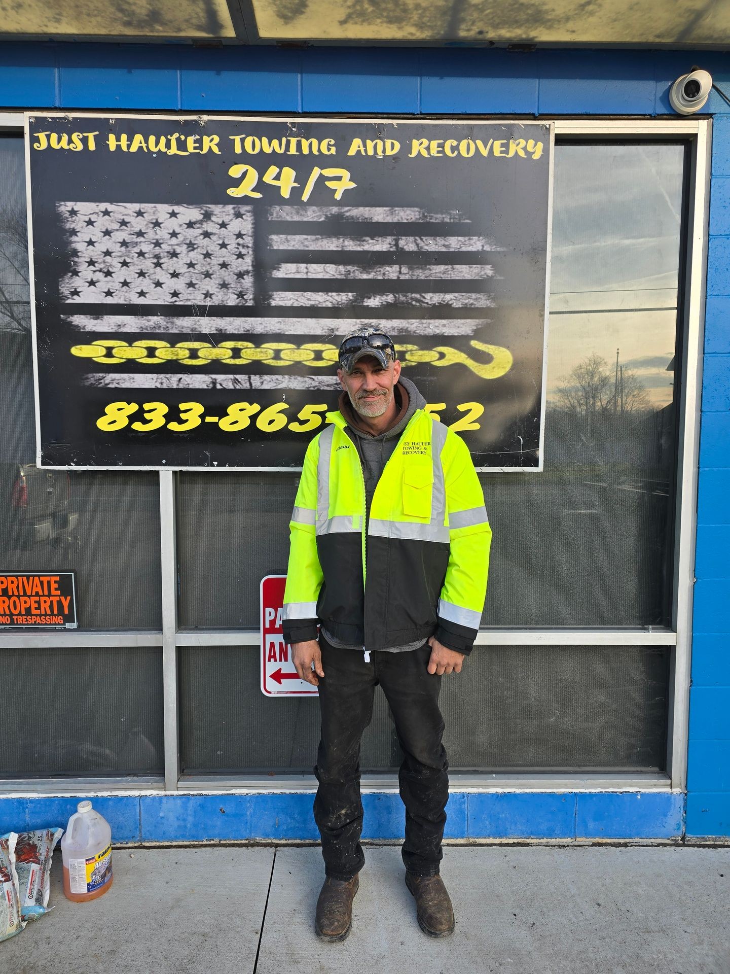 Person in high-visibility jacket standing in front of a towing and recovery service sign.