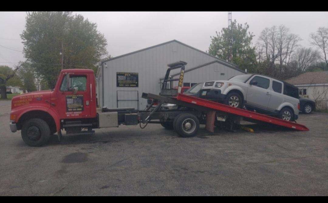 Red tow truck loading a silver SUV onto its flatbed in a parking lot.