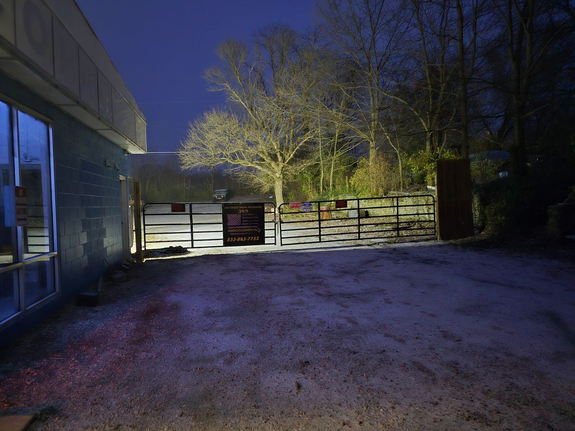 Night view of an illuminated gate and building exterior with surrounding bare trees.